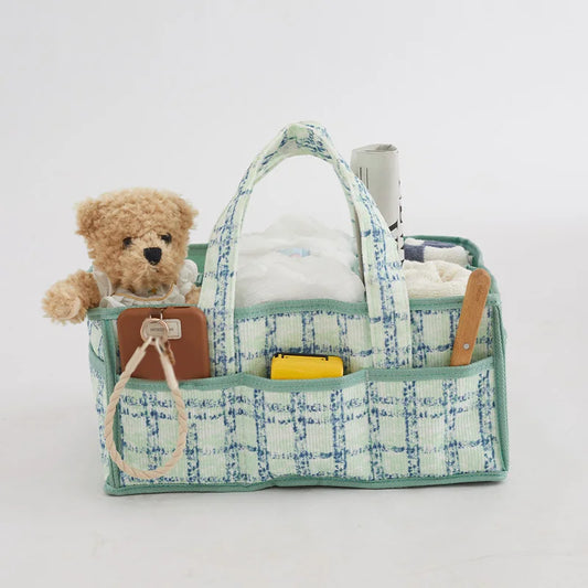 Portable baby diaper caddy in green and blue plaid fabric, with a teddy bear, diapers, and accessories.