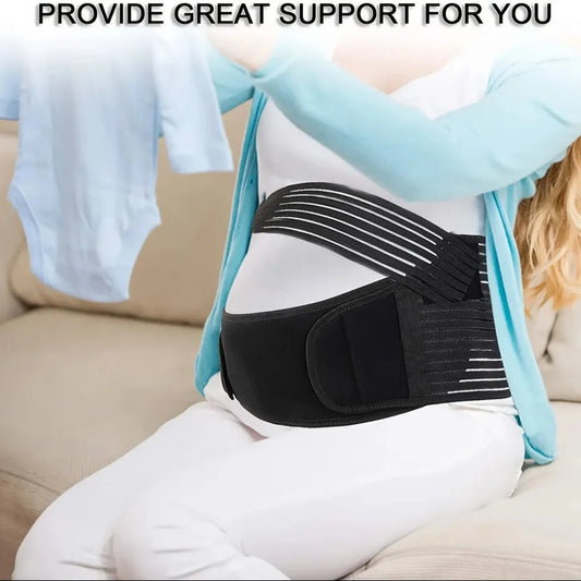 Pregnant woman wearing a black adjustable maternity support belt with white elastic straps, holding baby clothes.
