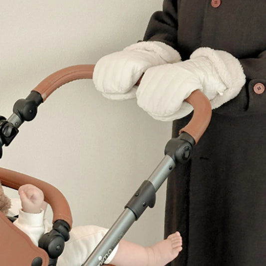 White fleece-lined stroller mittens on a brown handlebar, keeping hands warm while pushing a baby.