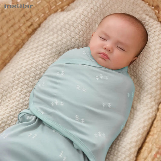 Sleeping baby swaddled in a light blue cotton sleep sack with white tree patterns.