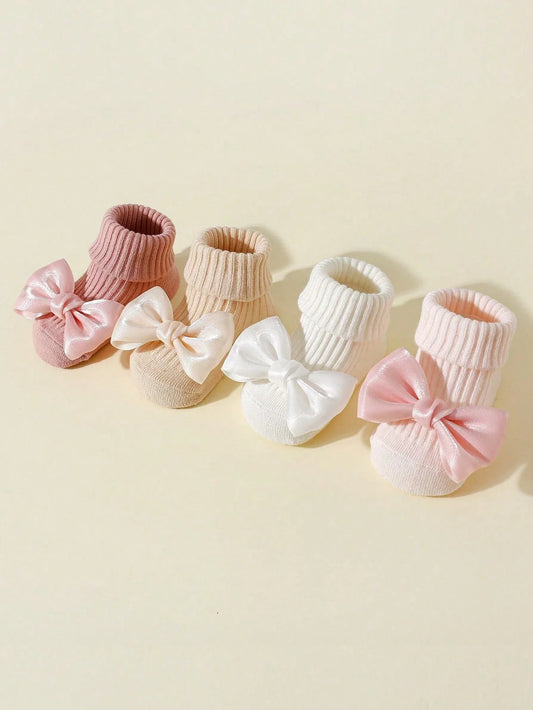 Four pairs of cotton baby socks with bows in pink, beige, white, and light pink, featuring anti-slip soles.