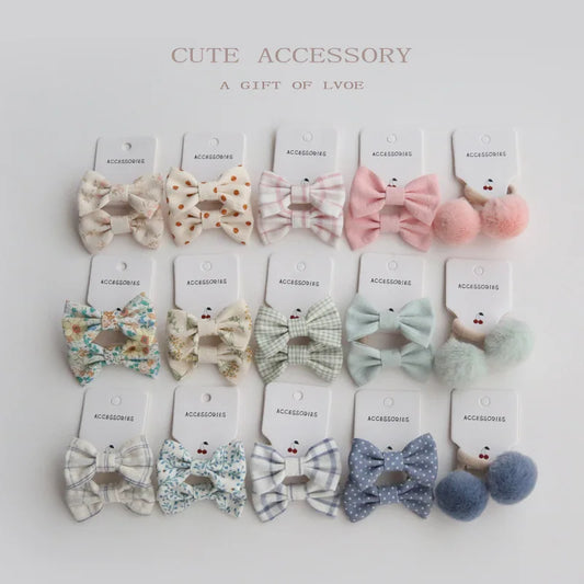 Set of 10 handmade elastic hair bows for girls in various pastel patterns and colors, including floral, plaid, polka dot, and pom-pom designs.