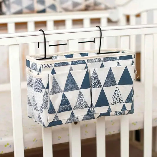 Cotton multi-compartment baby crib organizer with blue and white triangle pattern, hanging on a white crib.