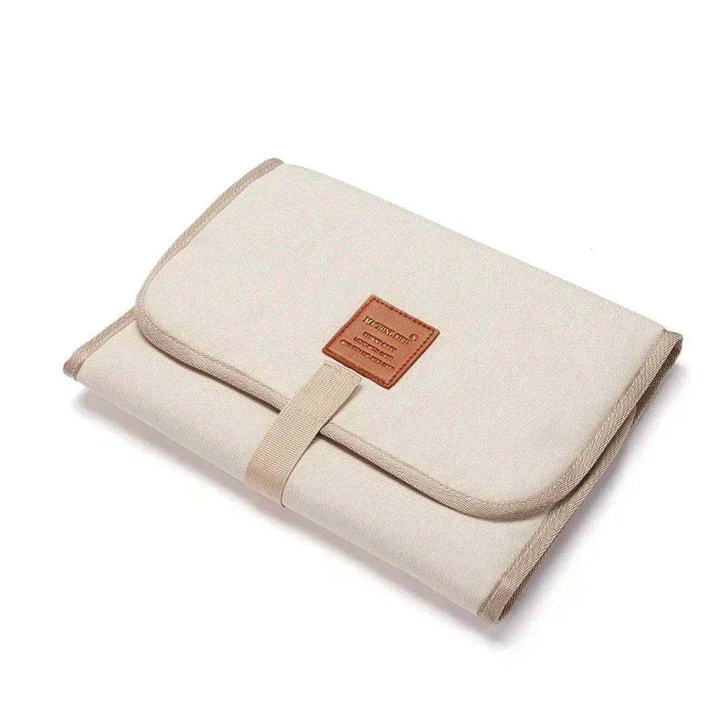 Foldable beige waterproof baby changing pad with a brown faux leather label and strap closure.