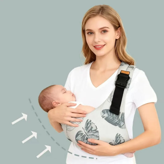 Woman holding a sleeping baby in a gray cotton crossbody baby carrier with a leaf pattern and adjustable strap.