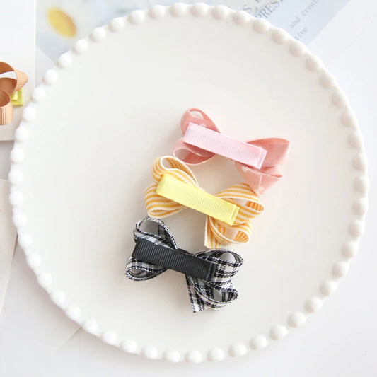 Set of three colorful bow hair clips for babies and girls: pink, yellow striped, and black plaid.