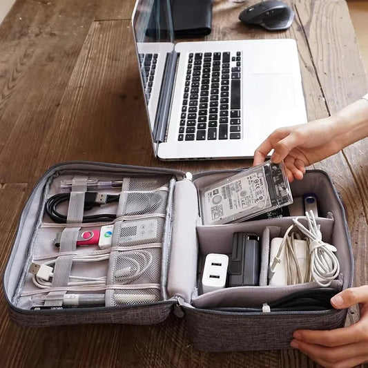 Gray waterproof oxford fabric organizer bag for electronic cables and accessories, with a laptop in the background.