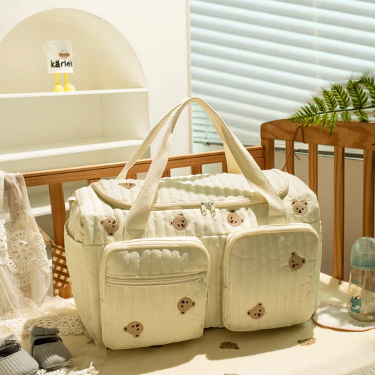 Quilted cream cotton diaper bag with embroidered teddy bears, zipper closure, and front pockets.