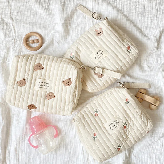 Three quilted cream cotton baby diaper bags with zippers, embroidered with bears, bunnies, and flowers.