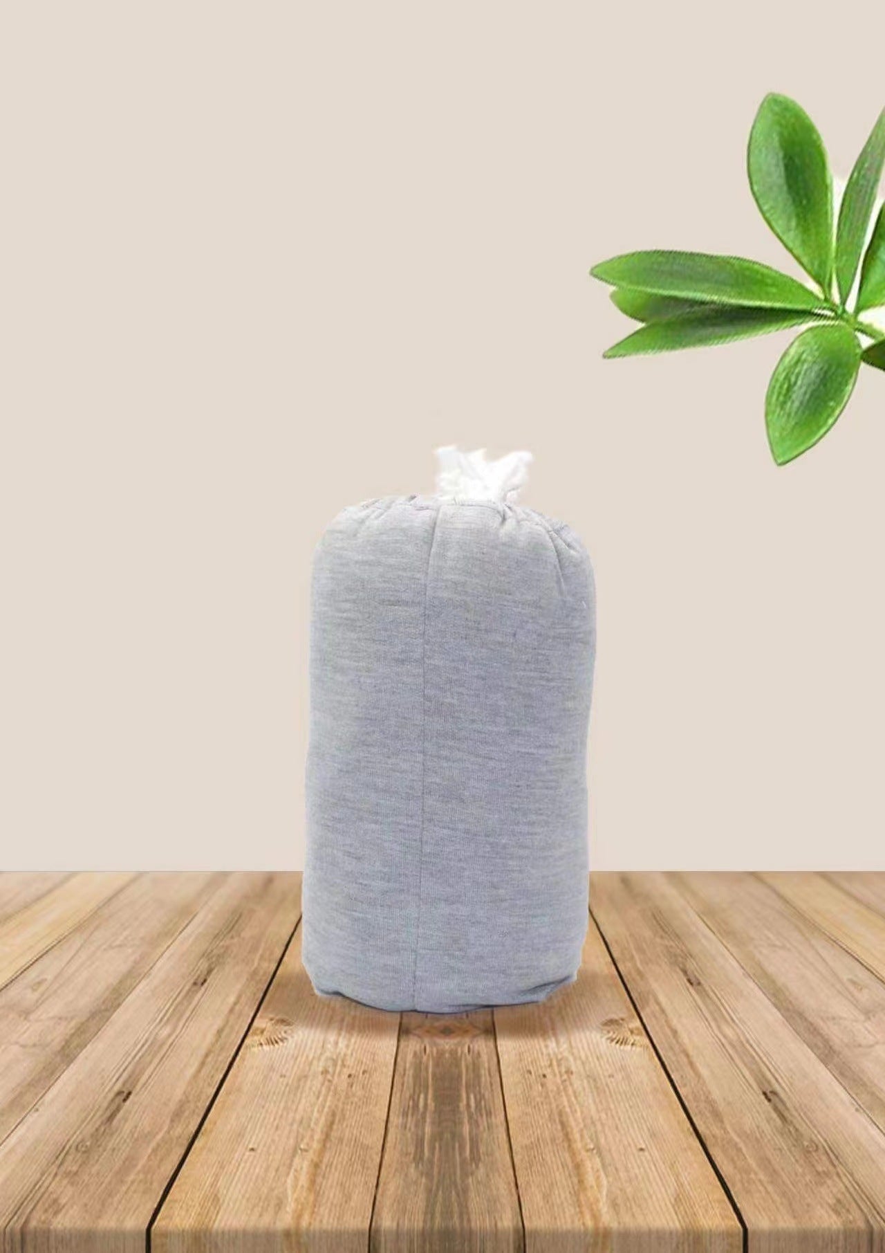 Soft gray cotton baby wrap carrier, folded and tied, on a wooden surface with green leaves.