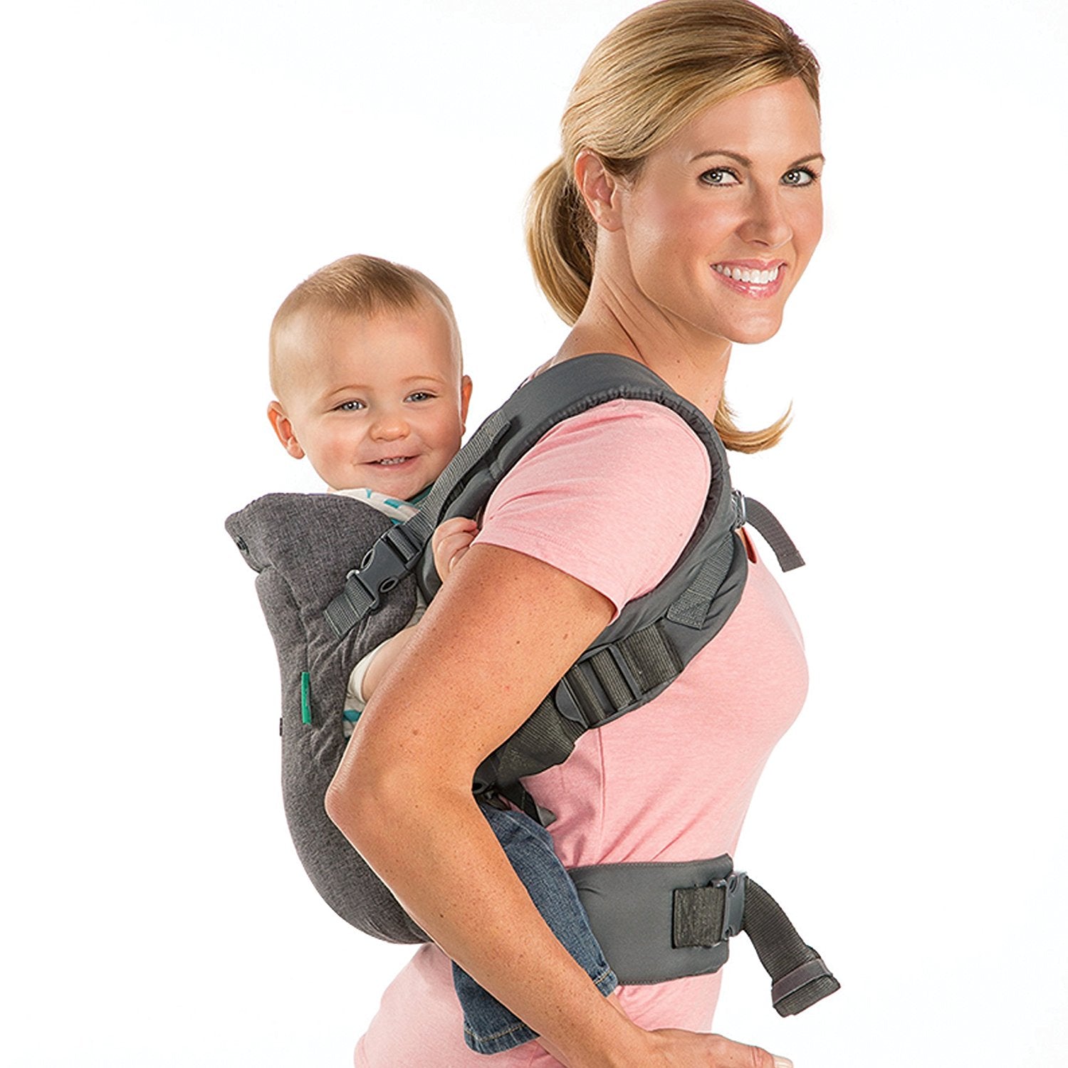 Smiling woman wearing a gray ergonomic baby carrier with a happy baby on her back.