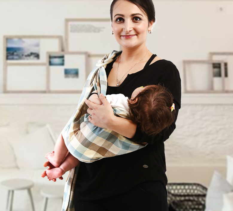 Smiling woman holding a baby in a soft, breathable plaid cotton baby sling carrier.