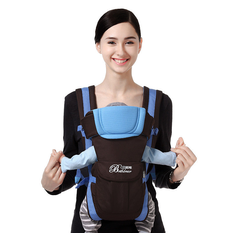 Smiling woman carrying a baby in a brown and blue ergonomic, breathable baby carrier.