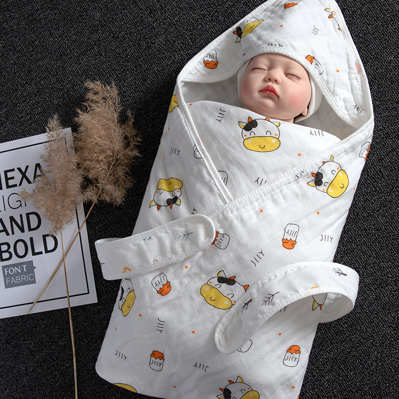 White cotton gauze baby swaddle with cute cow print, wrapped around a doll.