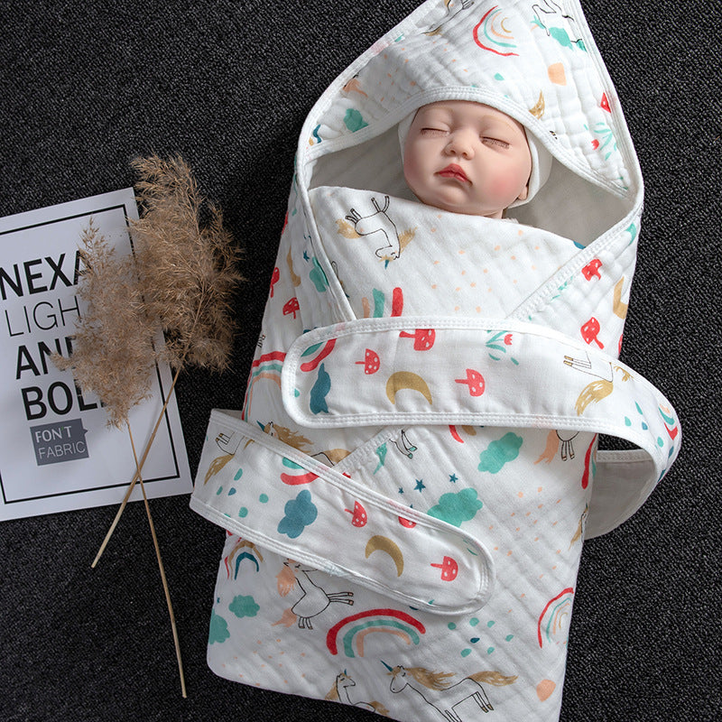 White cotton gauze baby swaddle with hood, colorful unicorn and rainbow print, and hook-and-loop closure.