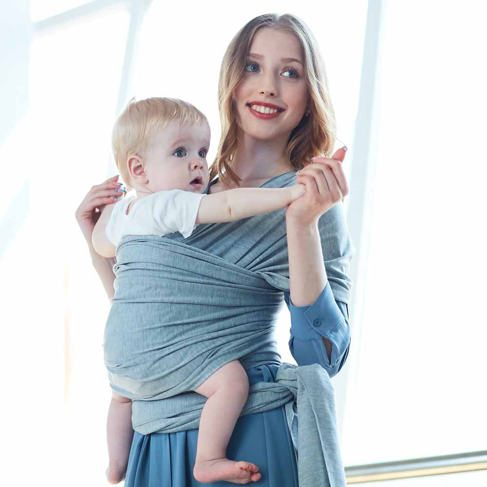 Smiling woman wearing a soft gray cotton baby wrap with a baby facing forward.