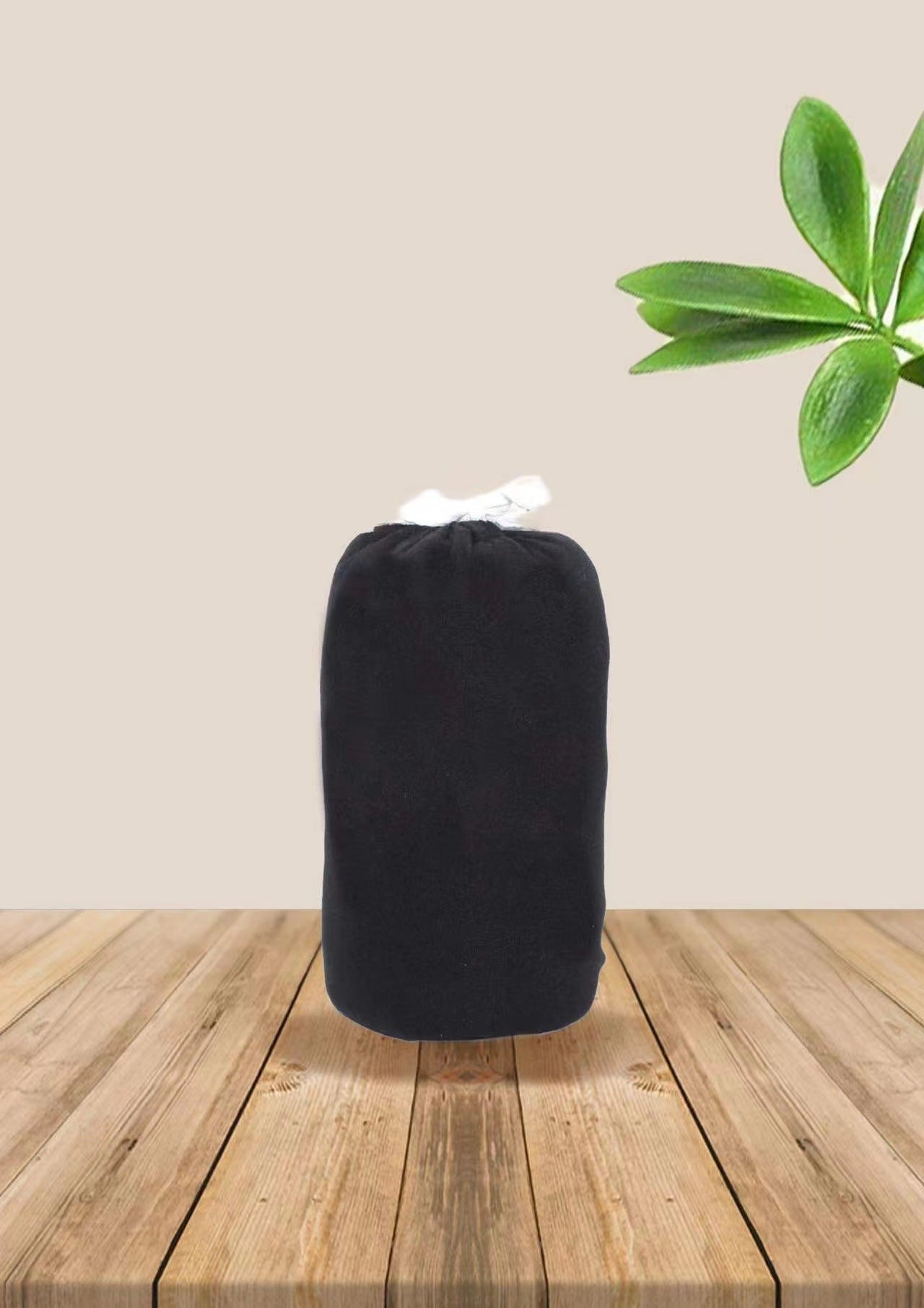 Folded black soft ergonomic baby wrap carrier, tied with a white string, on a wooden surface.