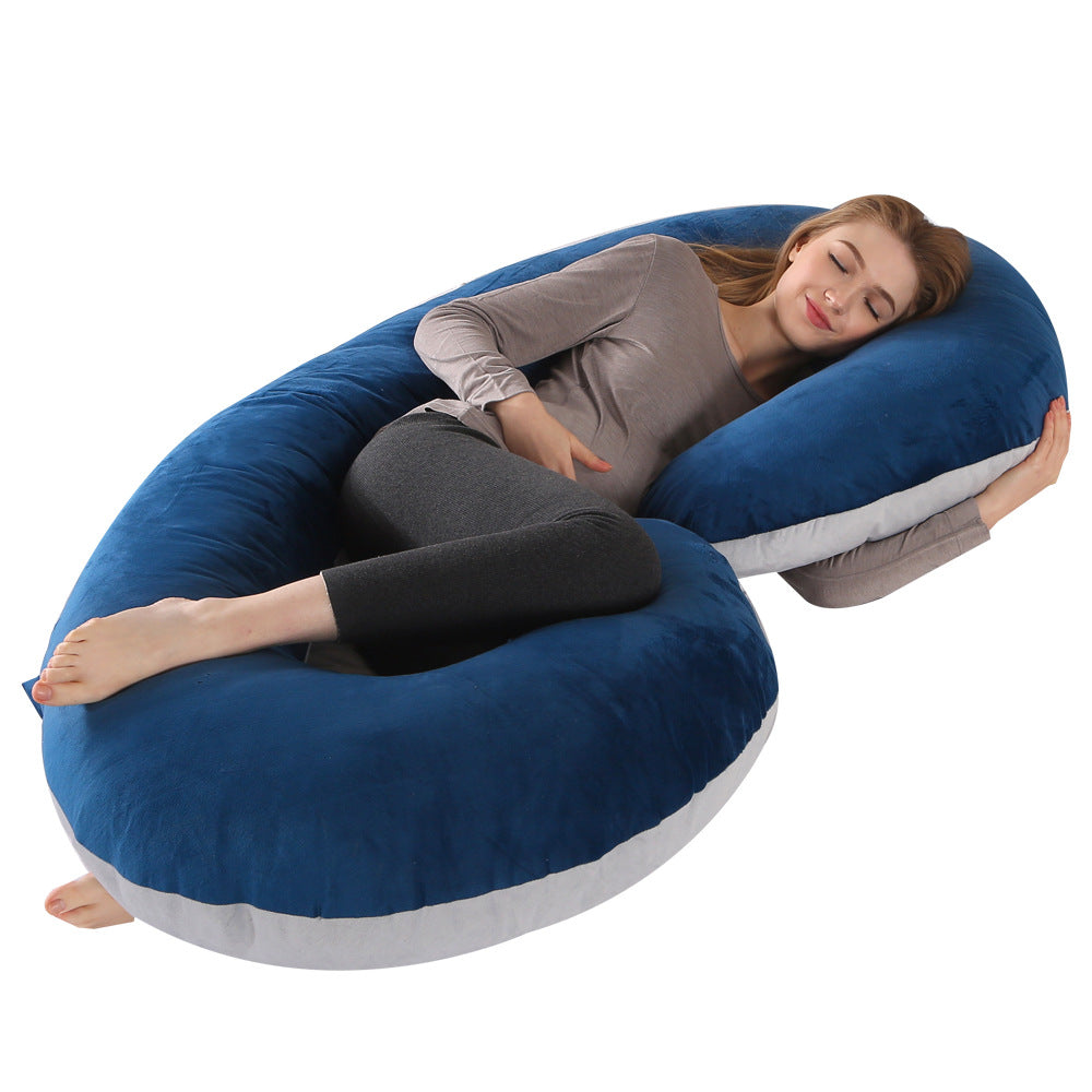 Pregnant woman sleeping comfortably on a large blue velvet C-shaped full body pillow with white trim.