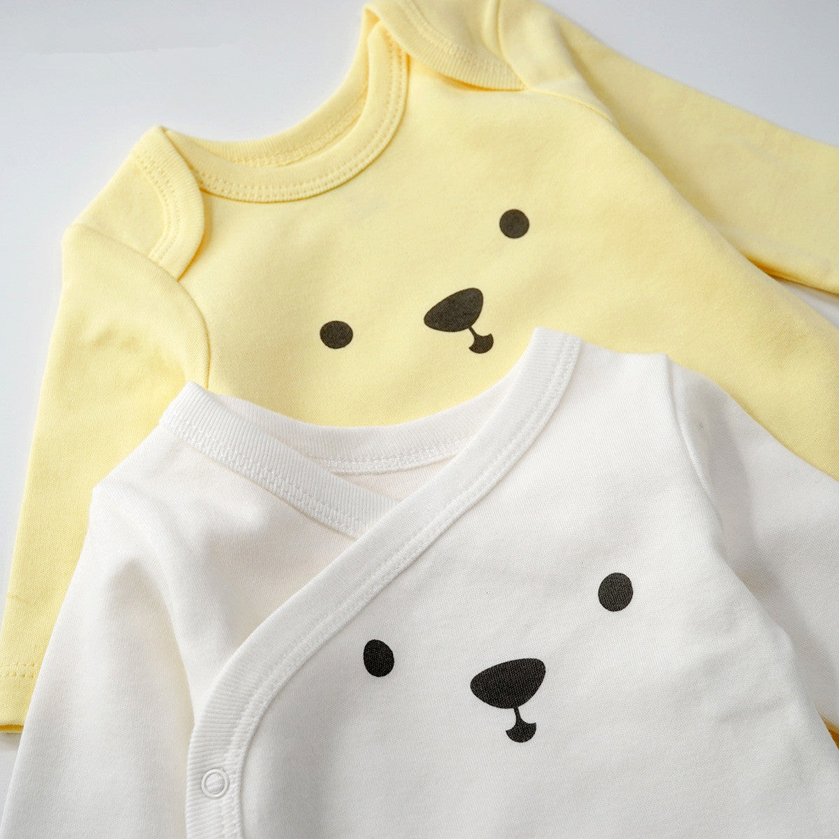 Two soft 100% cotton baby bodysuits, one yellow and one white, with cute bear face designs.