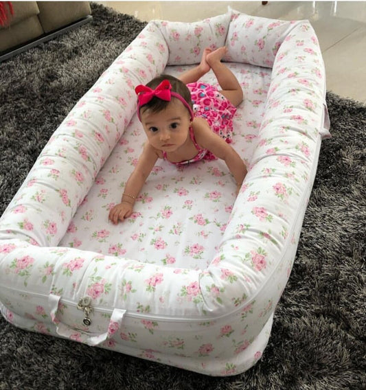 Portable cotton baby nest with pink floral print, a baby inside, and padded head protection.
