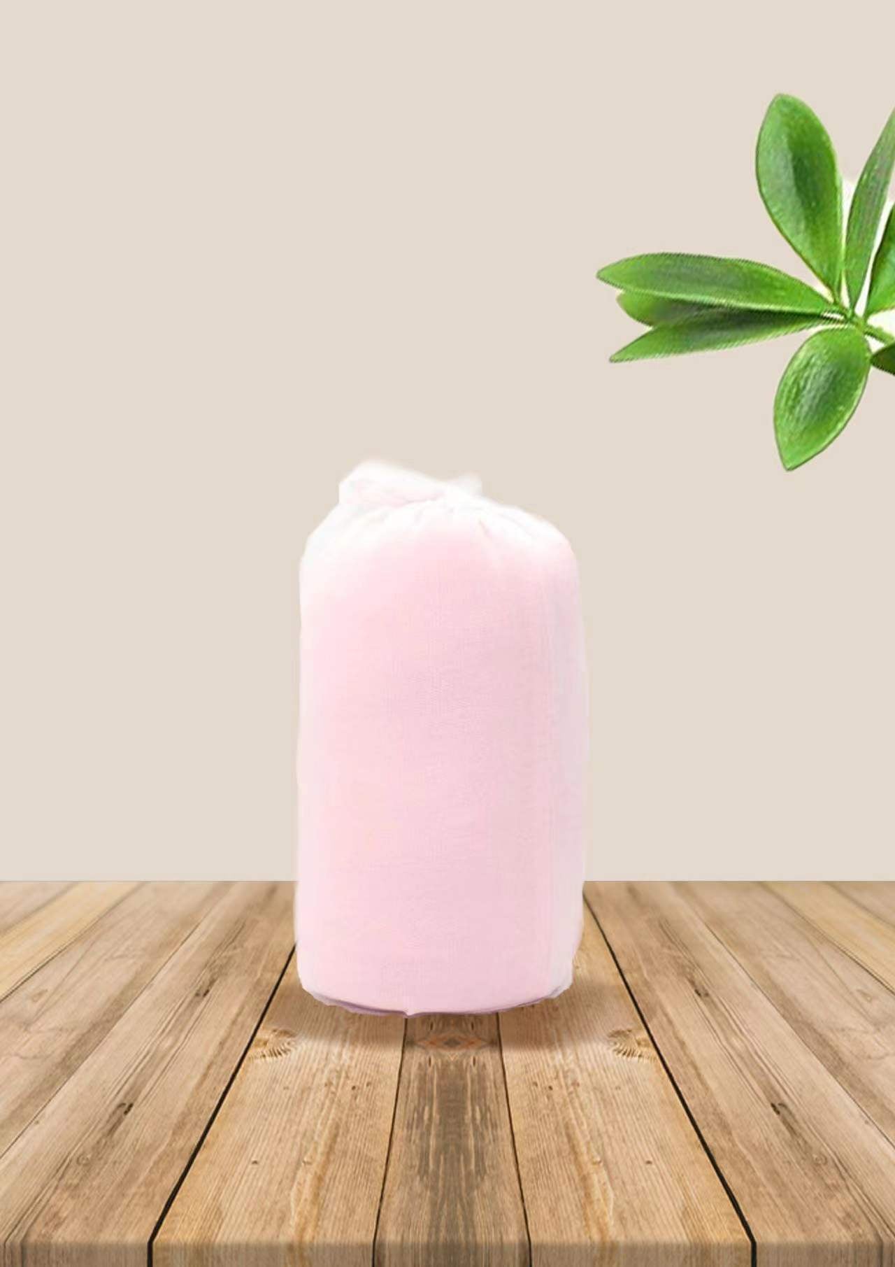 Soft pink ergonomic baby wrap carrier, folded and packaged, on a wooden table with green leaves.