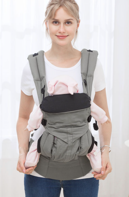 Woman wearing a gray ergonomic baby carrier with a pink doll, showcasing adjustable straps and breathable cotton.