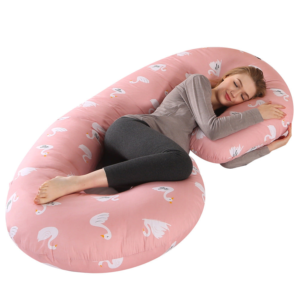 Pregnant woman sleeping soundly on a pink C-shaped full body pillow with white swan print.