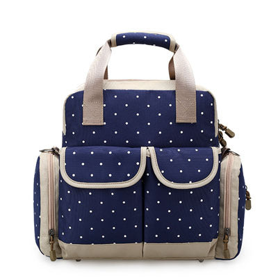 Navy blue polka dot diaper backpack with beige trim, multiple pockets, and top handles.