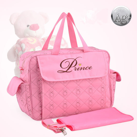 Pink polyester diaper bag with "Prince" embroidery, quilted teddy bear pattern, side pockets, and matching changing pad.