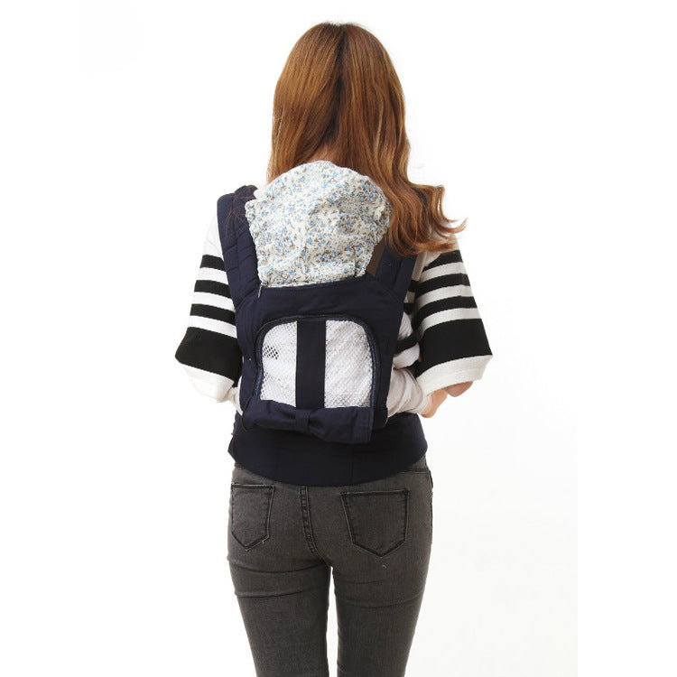 Woman from behind wearing a navy ergonomic baby carrier with a breathable mesh front and floral hood.