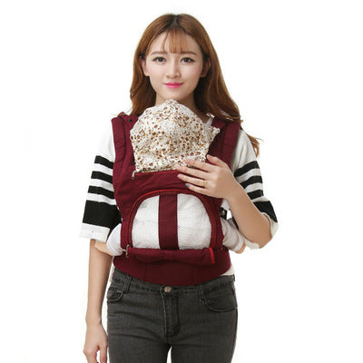 Woman wearing a maroon ergonomic baby carrier with a breathable mesh panel and a patterned hood.