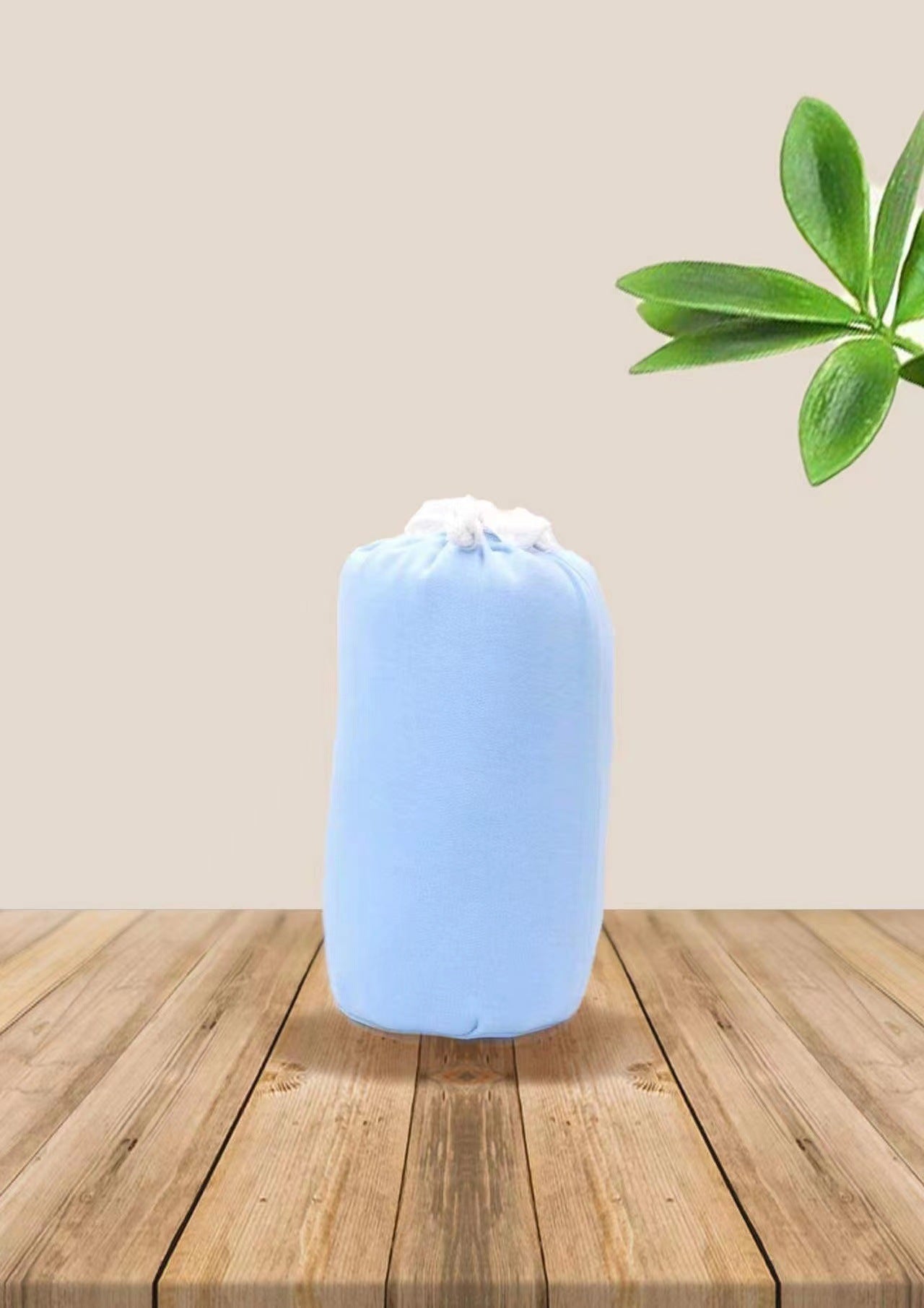 Soft blue ergonomic baby wrap carrier, rolled up on a wooden surface with green leaves.