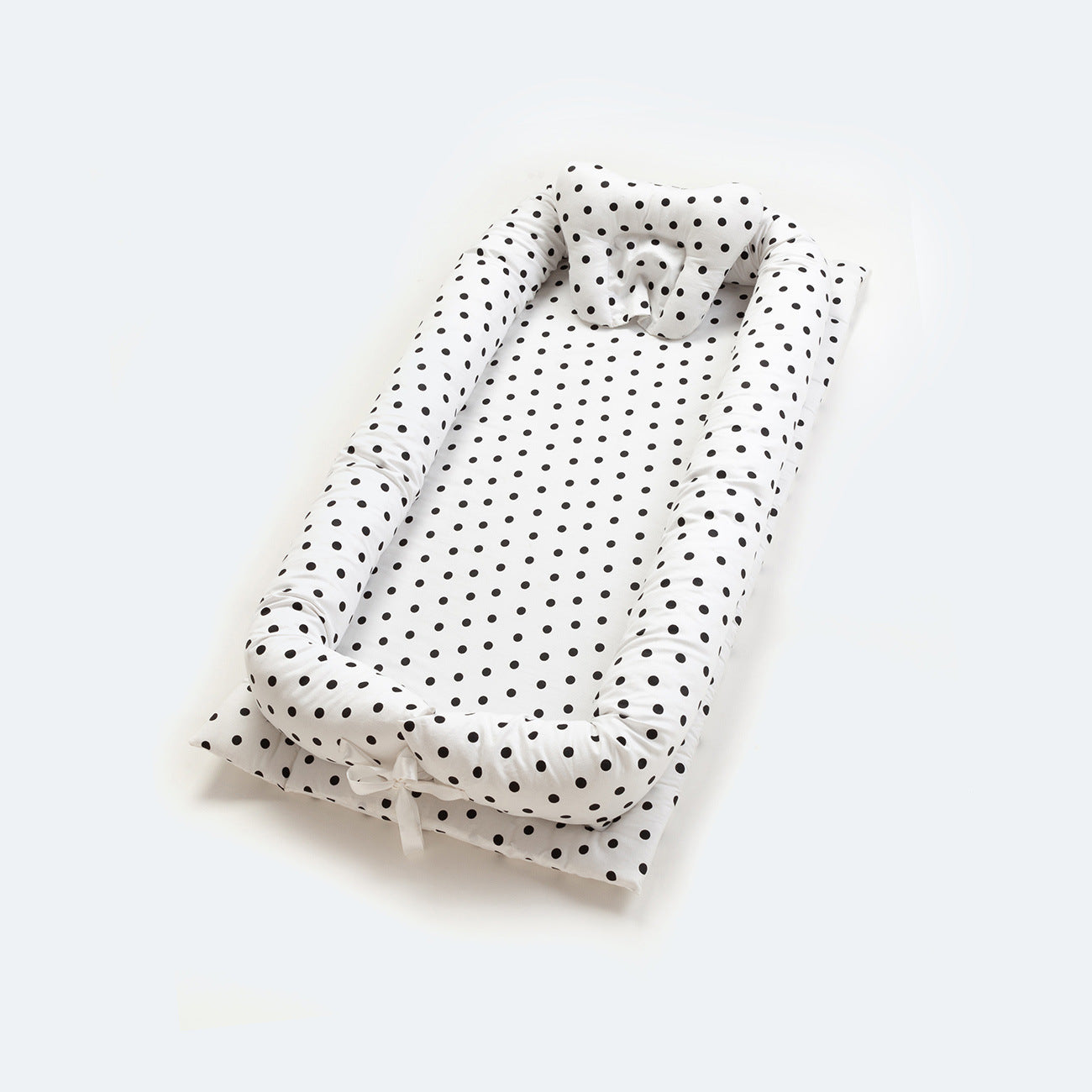 White cotton portable baby nest with black polka dots, padded sides, and head support.