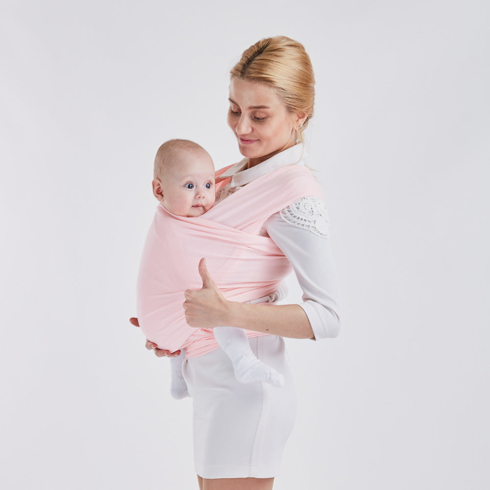 Mother holding baby in a soft pink cotton baby wrap carrier, giving a thumbs-up.