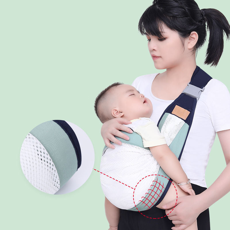 Woman carrying a sleeping baby in a sage green and navy ergonomic sling carrier with breathable mesh.