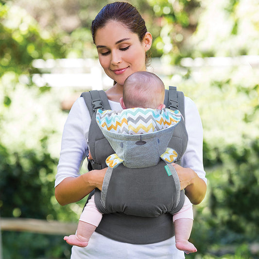 Woman carrying baby in a gray ergonomic carrier with a colorful chevron-patterned hood.