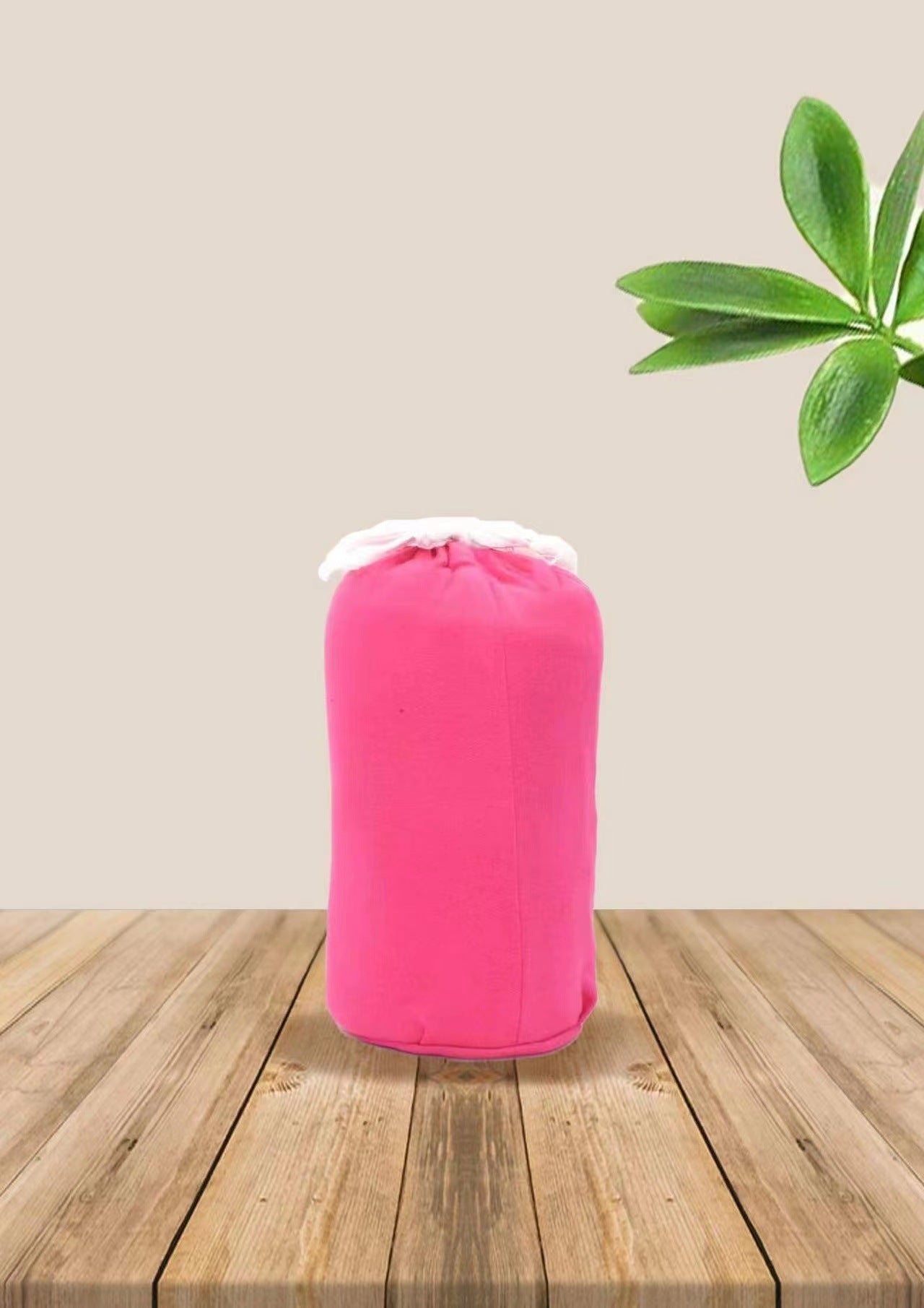 Pink soft ergonomic baby wrap carrier, rolled up, with white trim, on a wooden surface.