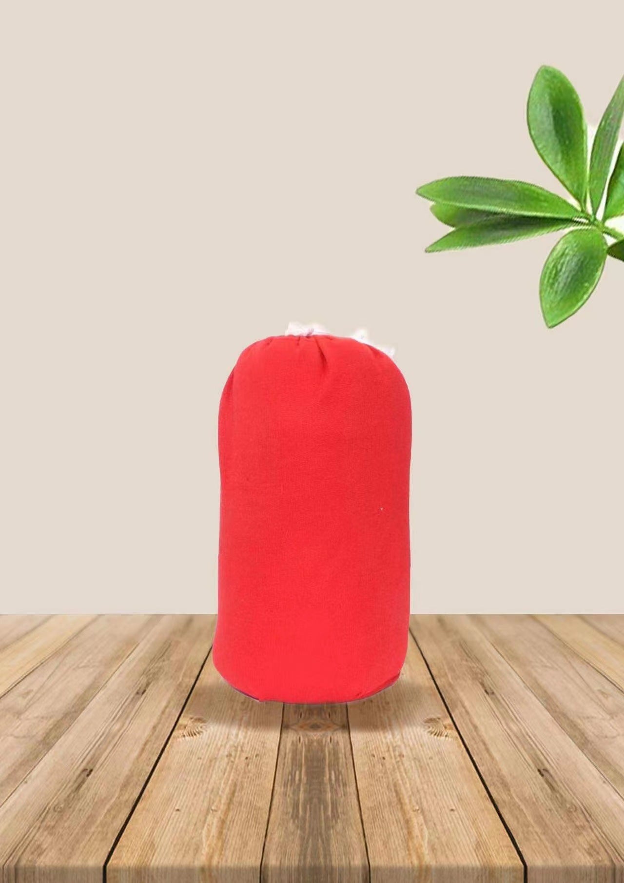 Red soft ergonomic baby wrap carrier, rolled up, on a wooden surface with a plant.