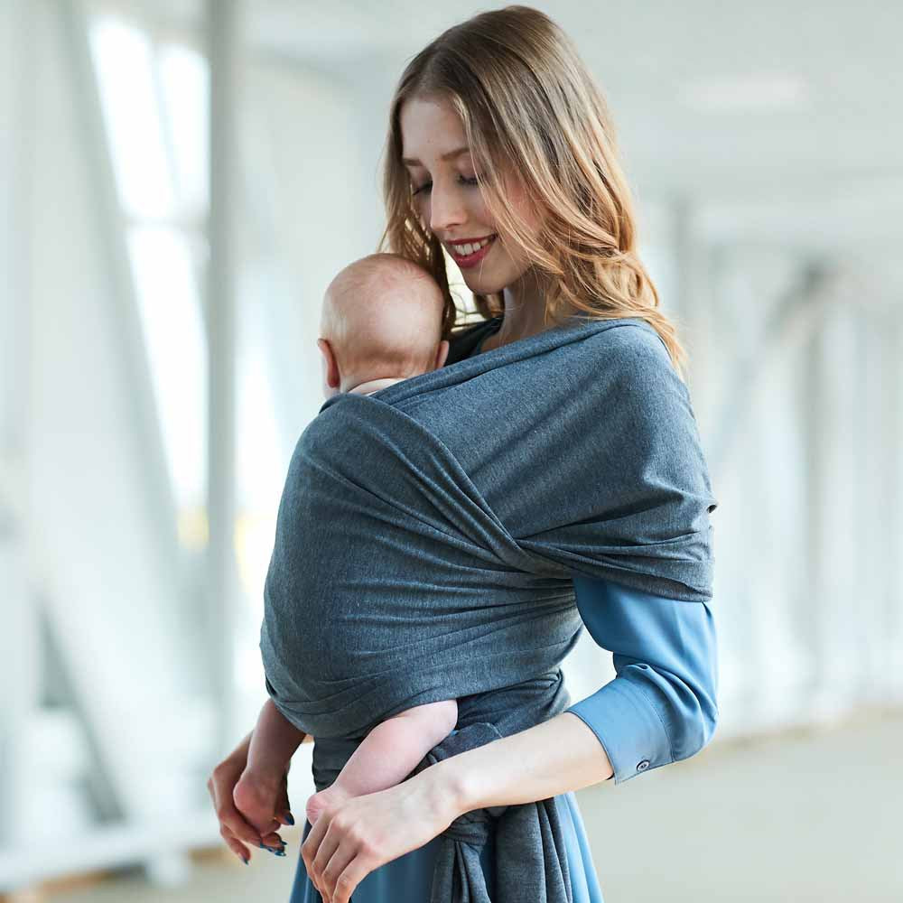 Smiling mother holding baby in a soft, gray cotton wrap carrier, promoting closeness and comfort.