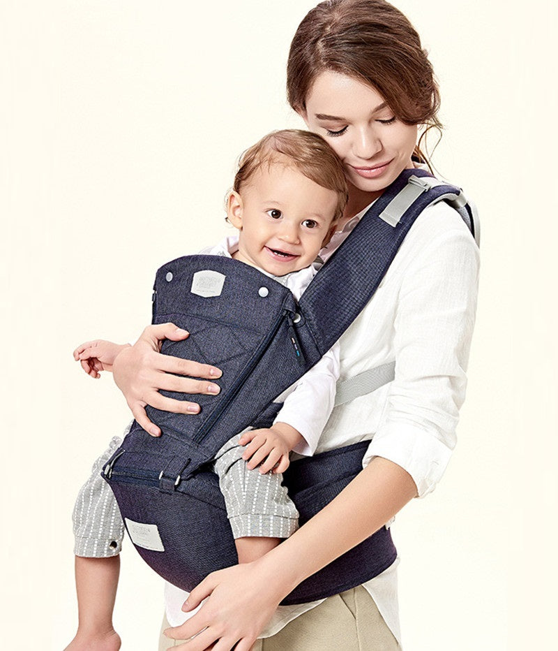 Woman carrying a smiling baby in a navy blue ergonomic hip seat carrier with quilted details.