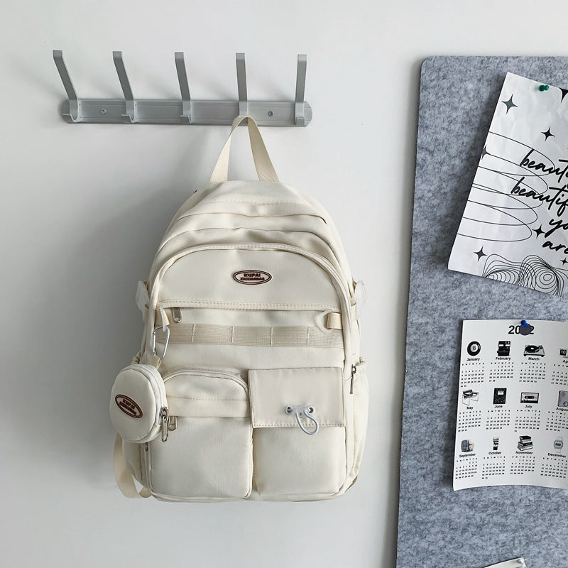 Cream nylon student backpack with multiple pockets, laptop compartment, and small matching pouch.