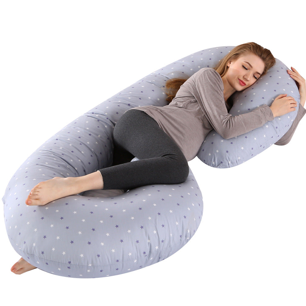 Pregnant woman sleeping soundly on a large, light blue C-shaped full body pillow with white stars.