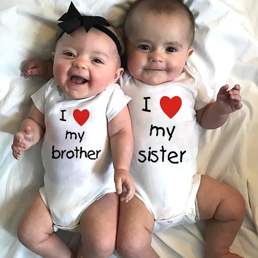 Two happy babies in white short-sleeve bodysuits with "I love my brother" and "I love my sister" prints.
