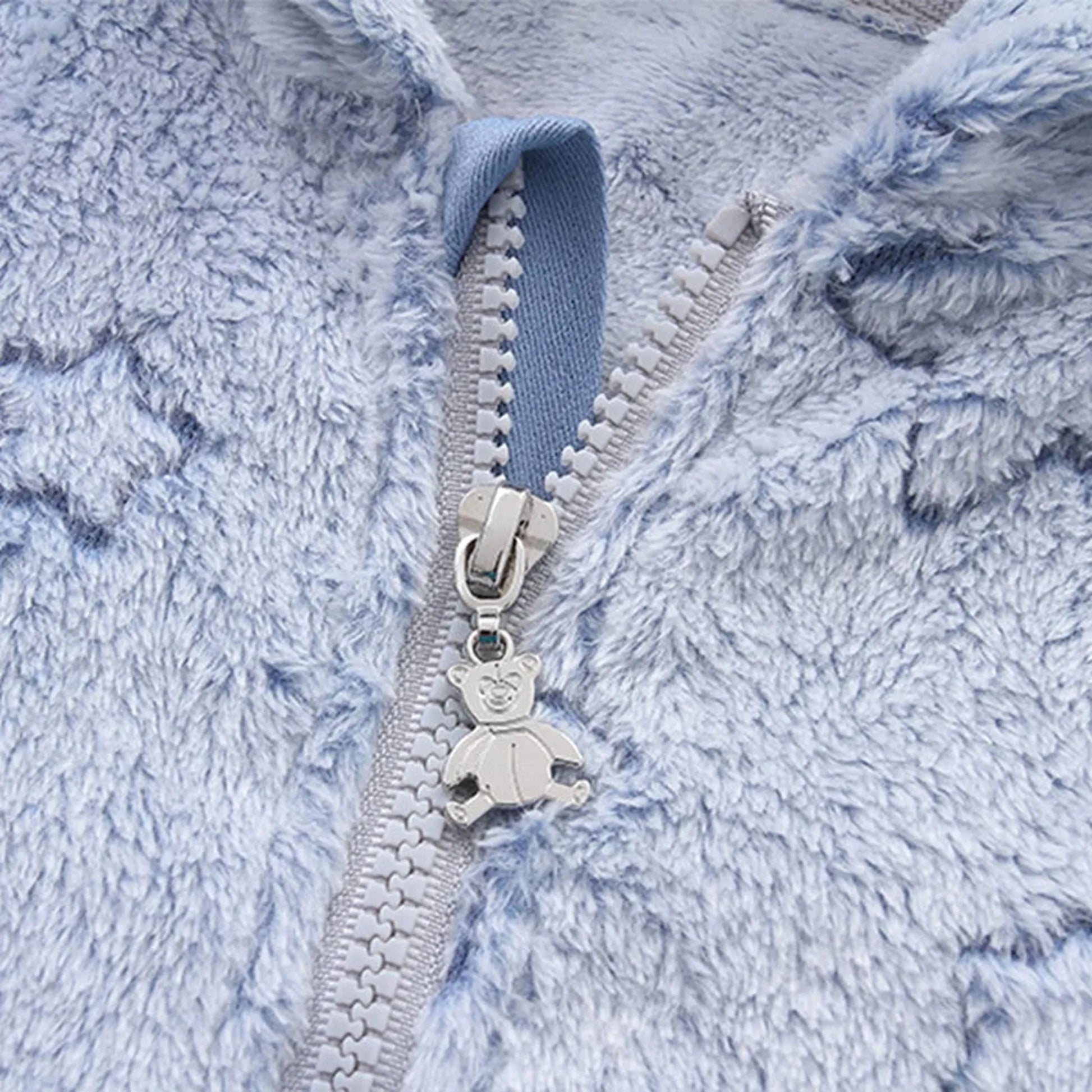 Close-up of a light blue fluffy flannel baby romper with a silver zipper and a cute bear-shaped pull.