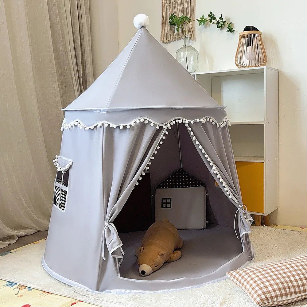 Foldable gray cotton castle play tent for kids with pom-pom trim, window, and open entrance.