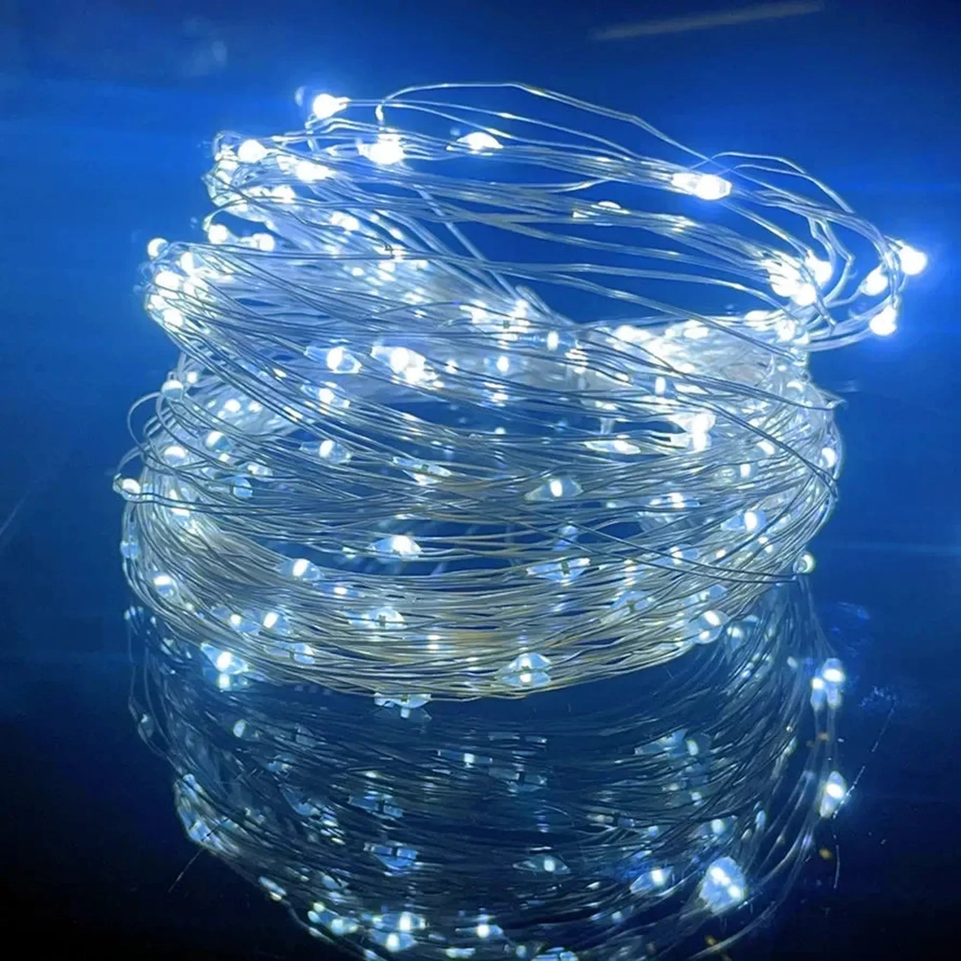 Coiled string of bright white LED fairy lights on a thin copper wire, reflecting on a dark blue surface.