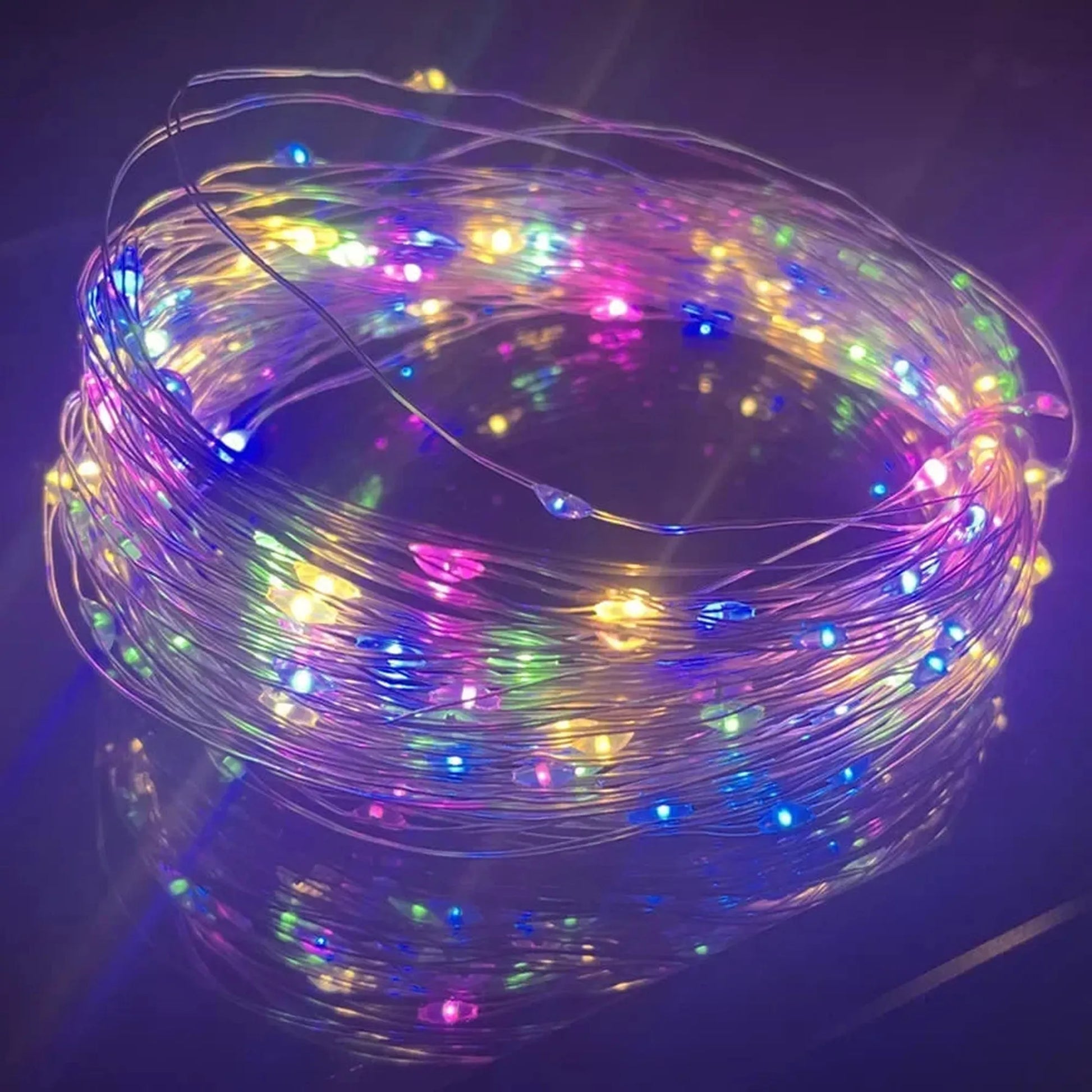 Coiled multicolor LED string lights with tiny bulbs on a flexible copper wire, reflecting on a dark surface.