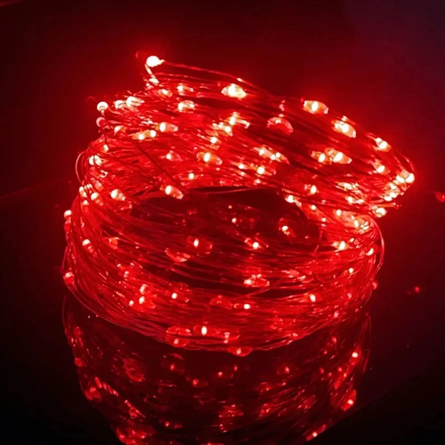 Coiled red LED string lights with a flexible copper wire, glowing brightly on a reflective surface.