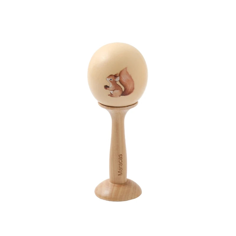 Wooden Montessori maraca with a cute squirrel illustration, natural wood handle, and "Maracas" engraved.