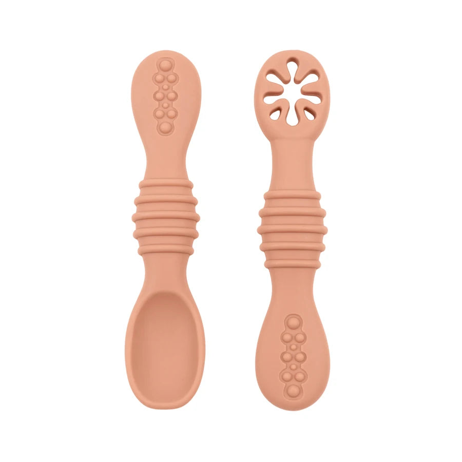Two peach silicone baby training spoons, one solid and one with a flower-shaped teether, for feeding.